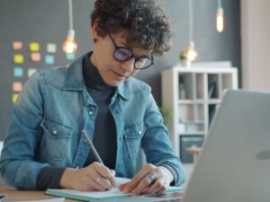 Woman with glasses writing in notebook at desk